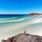 man standing on the rock of one of the best beaches in La Paz